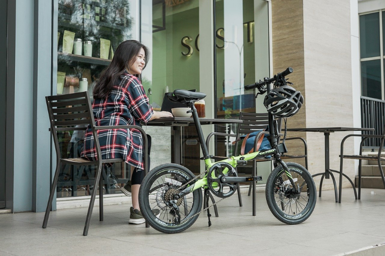 Une femme qui boit un café en terrasse, avec son vélo pliant posé contre la table