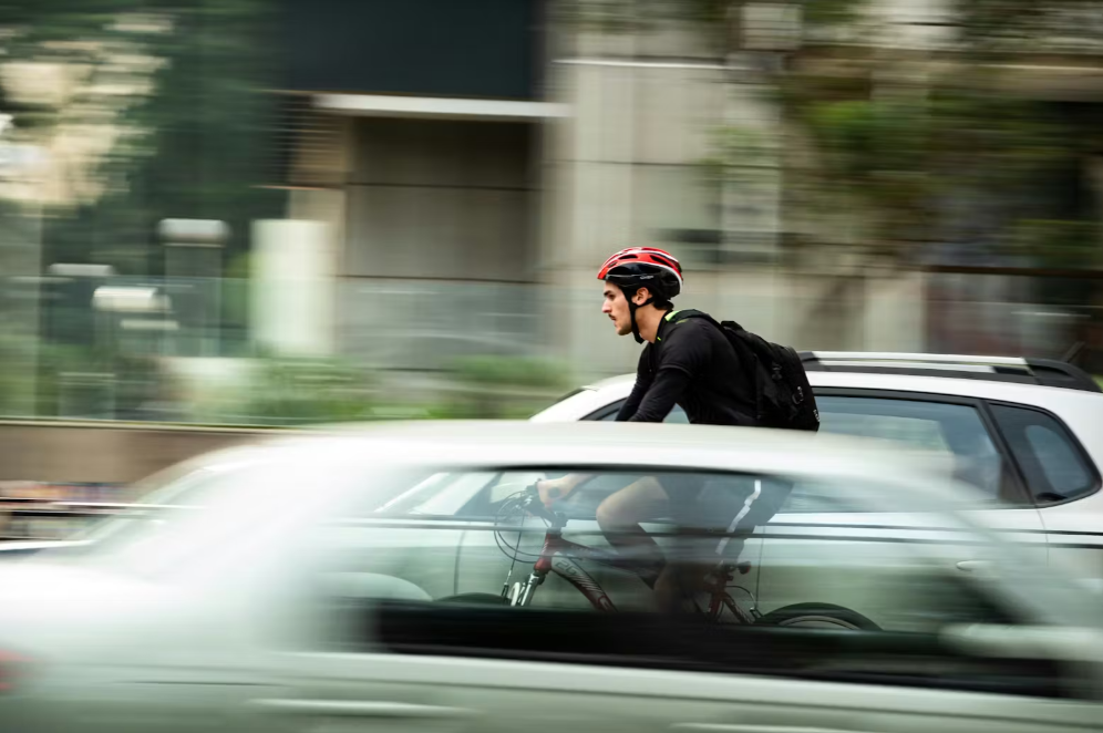 Un cycliste avec un casque vélo rouge qui circule en ville entre les voitures