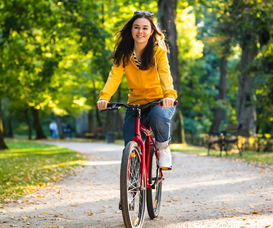 Femme souriante à vélo sur un chemin arboré dans un parc.