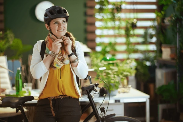 Une femme souriante, portant un casque de vélo, se tient dans un bureau avec des plantes.