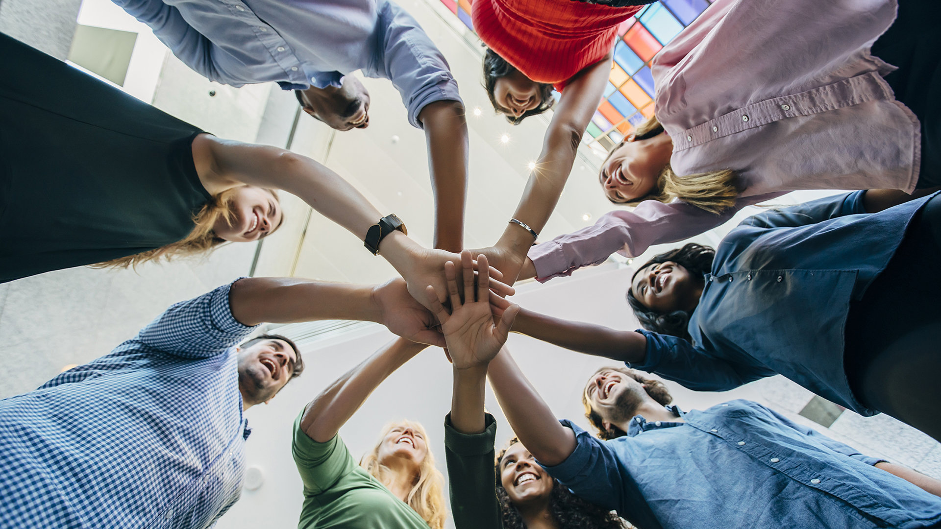 Groupe de personnes en cercle, mains réunies au centre, symbolisant la cohésion d'équipe.