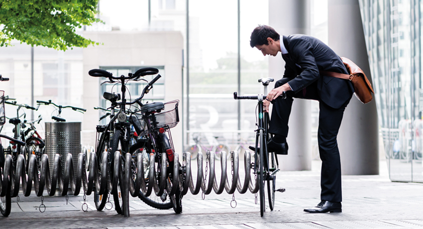 Un salarié attache son vélo à un parking extérieur, entouré de plusieurs autres vélos.