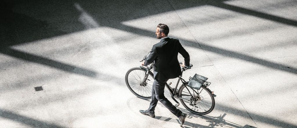 Un homme en costume marche à côté de son vélo sous une lumière d'intérieur tamisée.