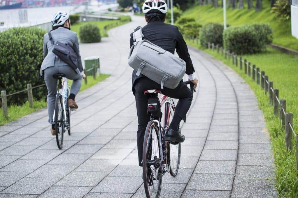 Deux vélotaffeurs circulant à vélo sur une piste cyclable bordée de verdure.