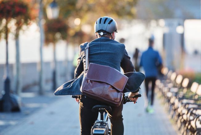 Un cycliste en tenue de ville roule dans une allée arborée.