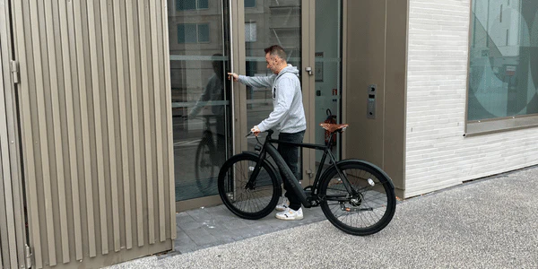 Un cycliste garé devant un bâtiment, tenant son vélo électrique tout en ouvrant une porte.