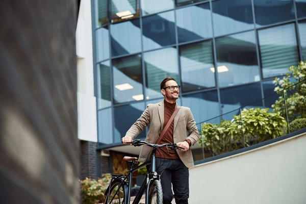 "Un homme souriant poussant son vélo devant un bâtiment moderne.