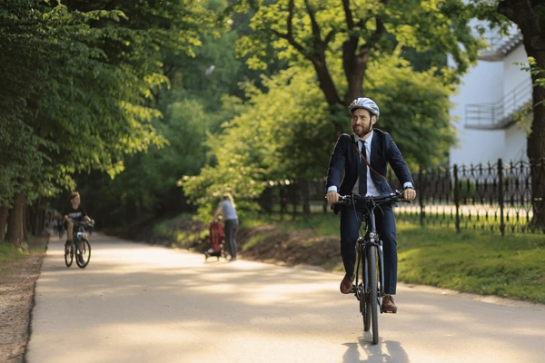 Un homme en costume, portant un casque, fait du vélo sur une piste cyclable ombragée