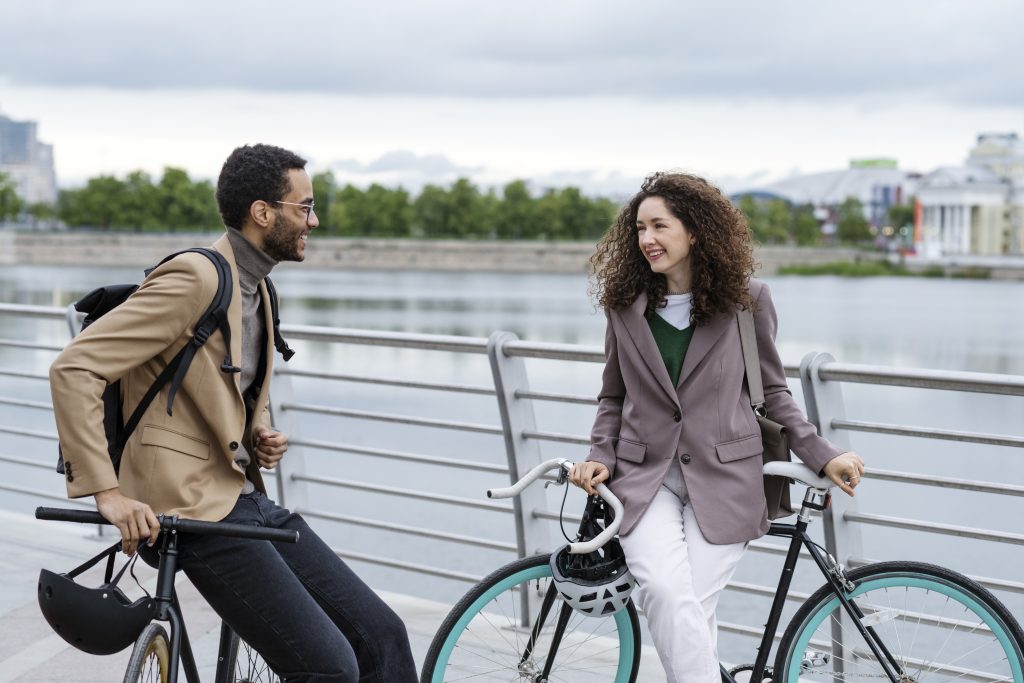 Un homme et une femme en tenue professionnelle échangent un sourire tout en s'arrêtant avec leurs vélos près d'un pont.