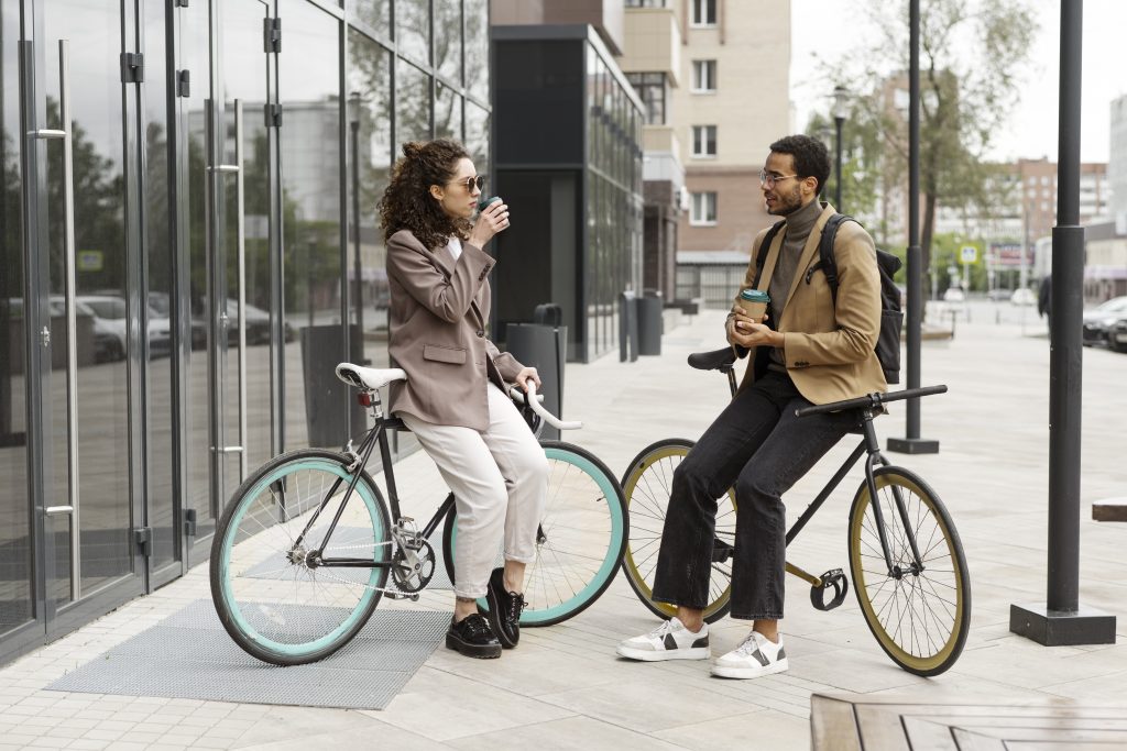 Deux collègues discutent devant un bâtiment tout en s'appuyant sur leurs vélos