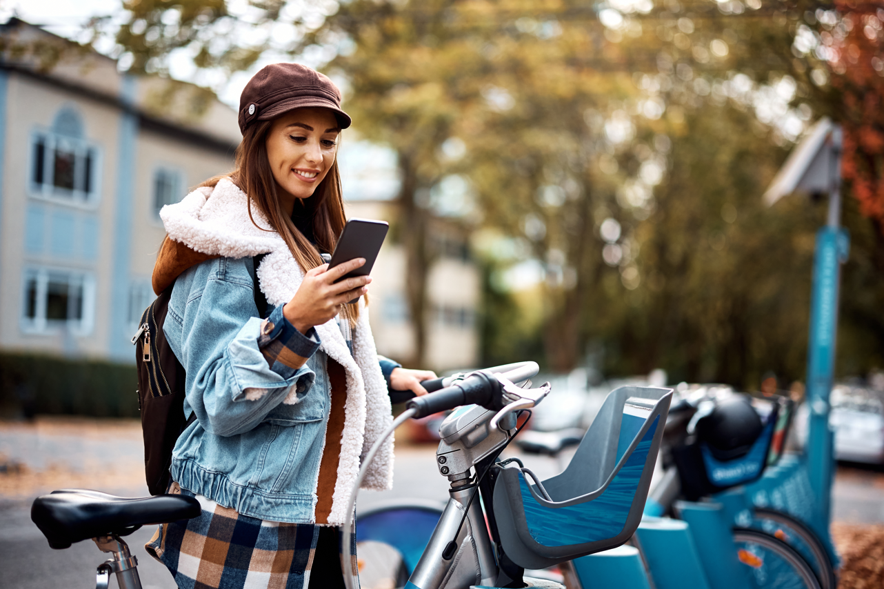 Une femme debout à côté de son vélo, dans la rue, qui consulte son téléphone